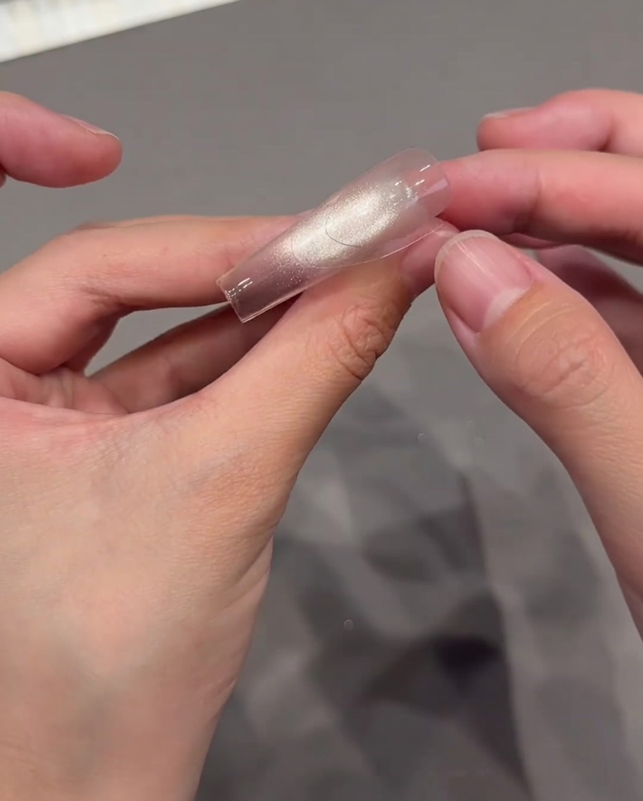 Pulgares colocando cuidadosamente una pegatina guía de punta francesa curvada y transparente sobre una uña brillante.