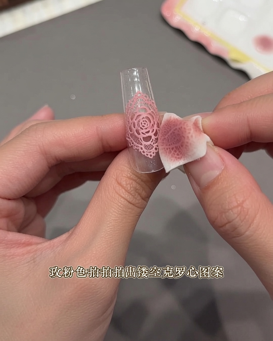 Primer plano de una mano usando una pequeña esponja de maquillaje para dar toques sobre una pegatina tipo encaje en una punta de uña clara.