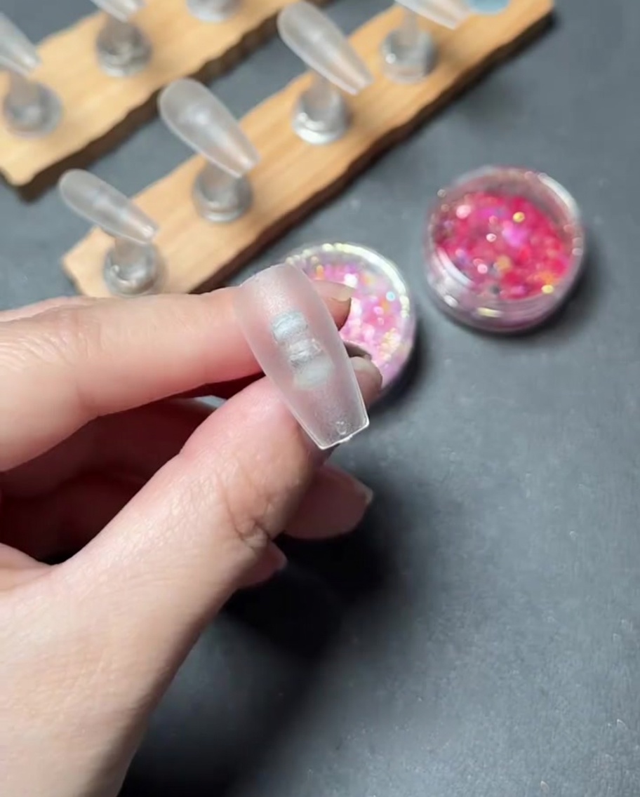 Un primer plano de un pincel aplicando gel base transparente sobre la superficie de una punta de uña de plástico transparente.