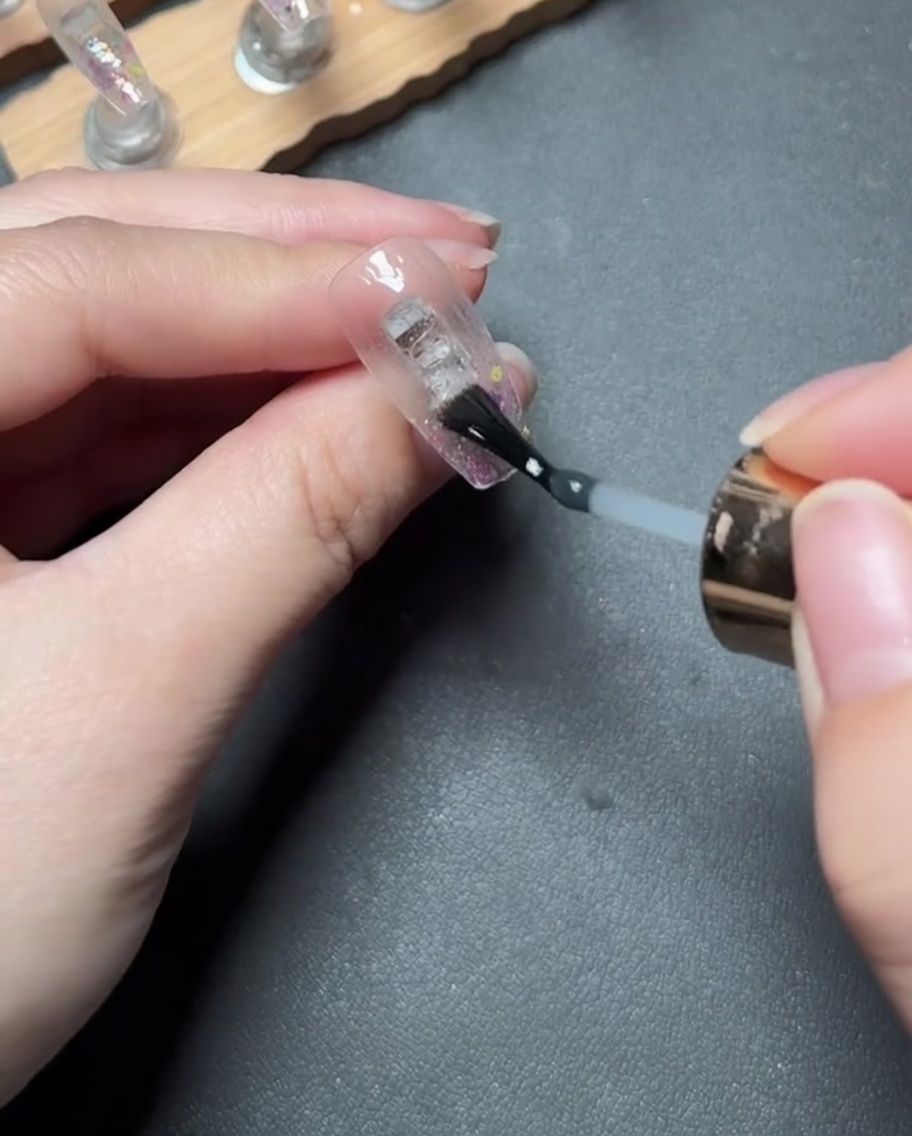 Aplicando un gel de refuerzo transparente y espeso sobre la punta de la uña cubierta de purpurina.