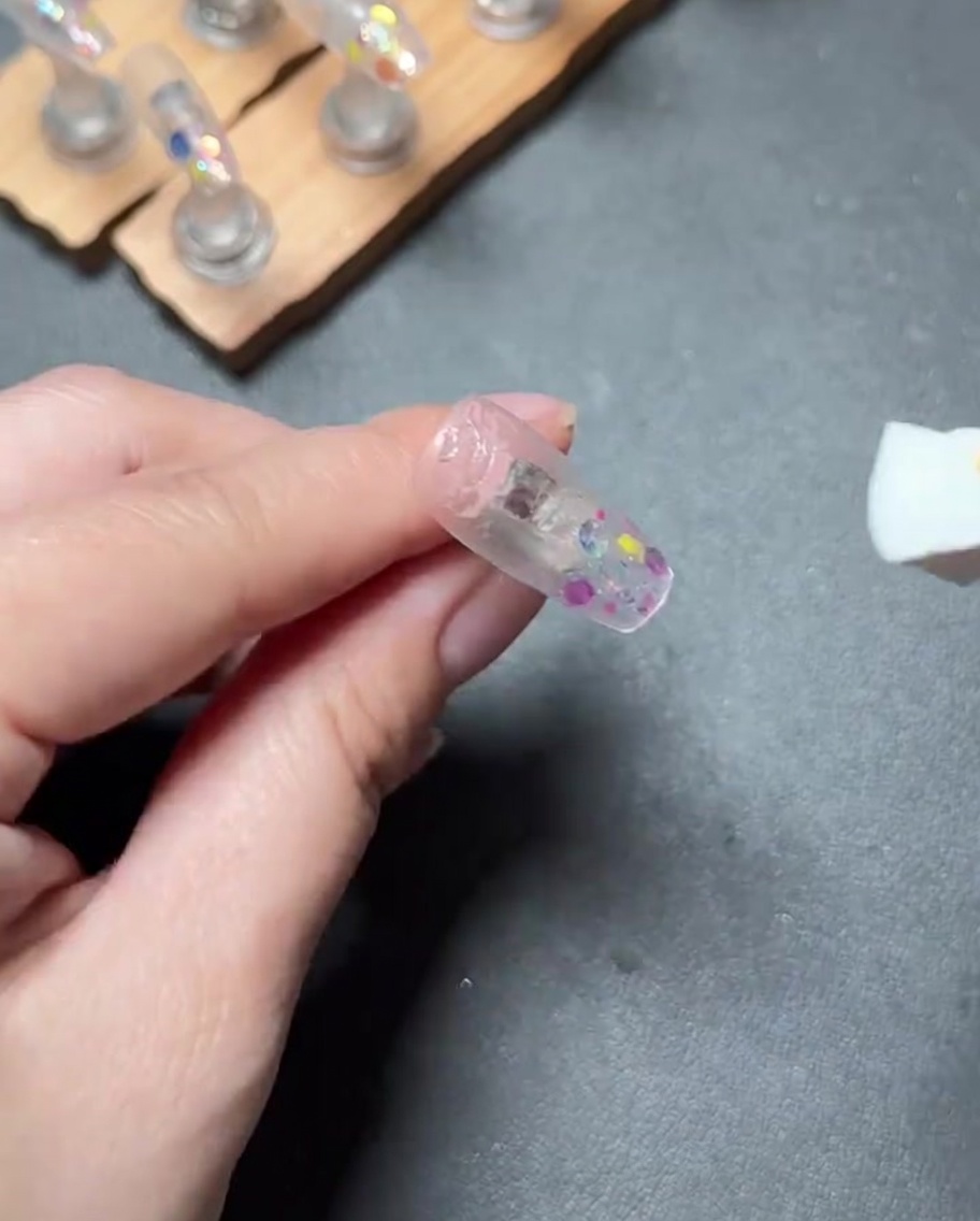 Una lima de uñas siendo utilizada para pulir la superficie de una uña postiza para crear un acabado liso.