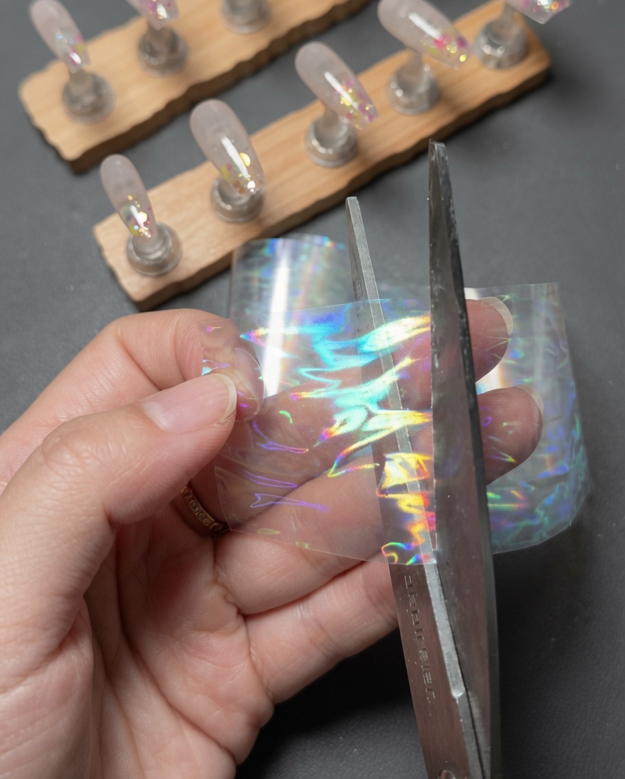 Manos usando tijeras para cortar un pequeño trozo rectangular de una tira de foil de transferencia láser aurora holográfico.
