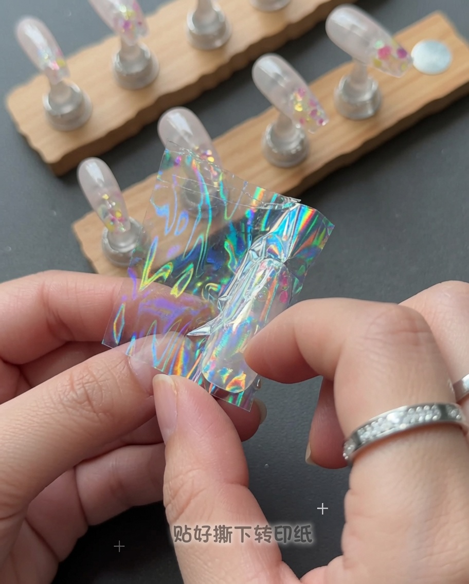 Una mano despegando una película de plástico transparente de una uña para revelar un diseño de estrella holográfico.