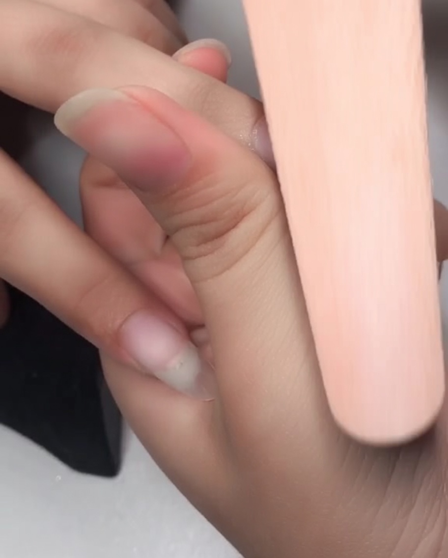 Primer plano de un bloque pulidor de uñas suavizando la superficie antes de la aplicación del gel.