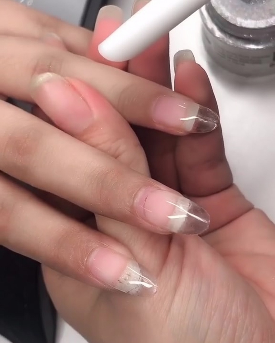 Un aplicador de silicona siendo utilizado para frotar polvo láser sobre la superficie de la uña.