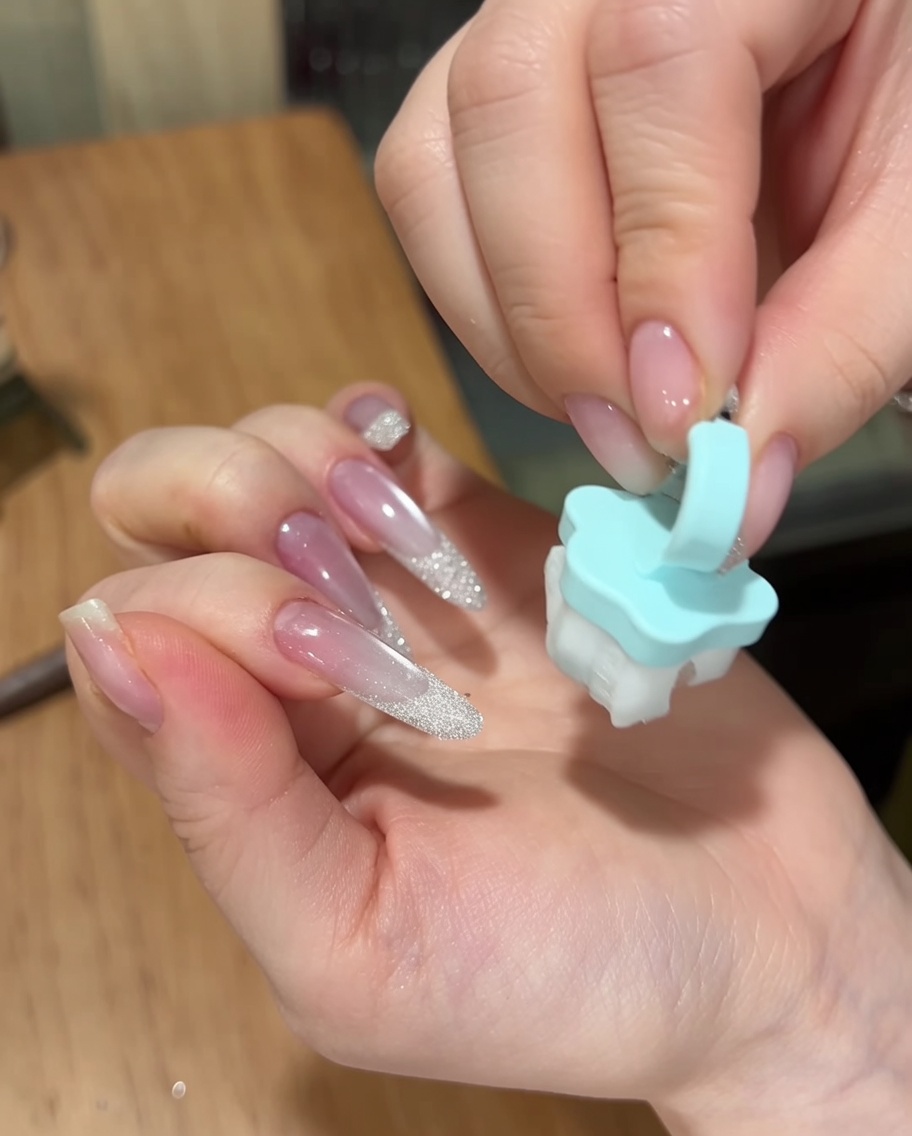 Una mano usando un pequeño pincel azul suave para desempolvar el exceso de polvo de azúcar de la superficie de una manicura terminada.
