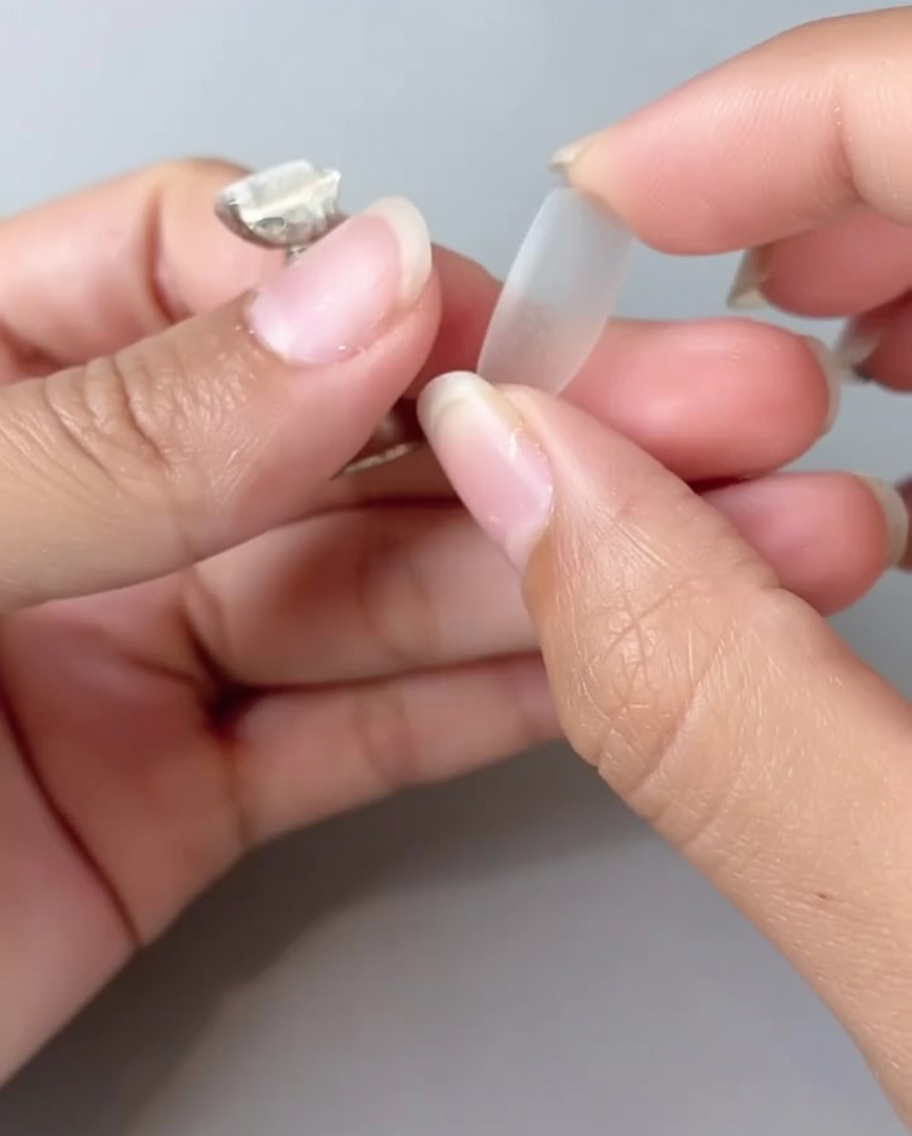 Primer plano de unos dedos sosteniendo un tip de uña transparente, girándolo para mostrar el reverso.