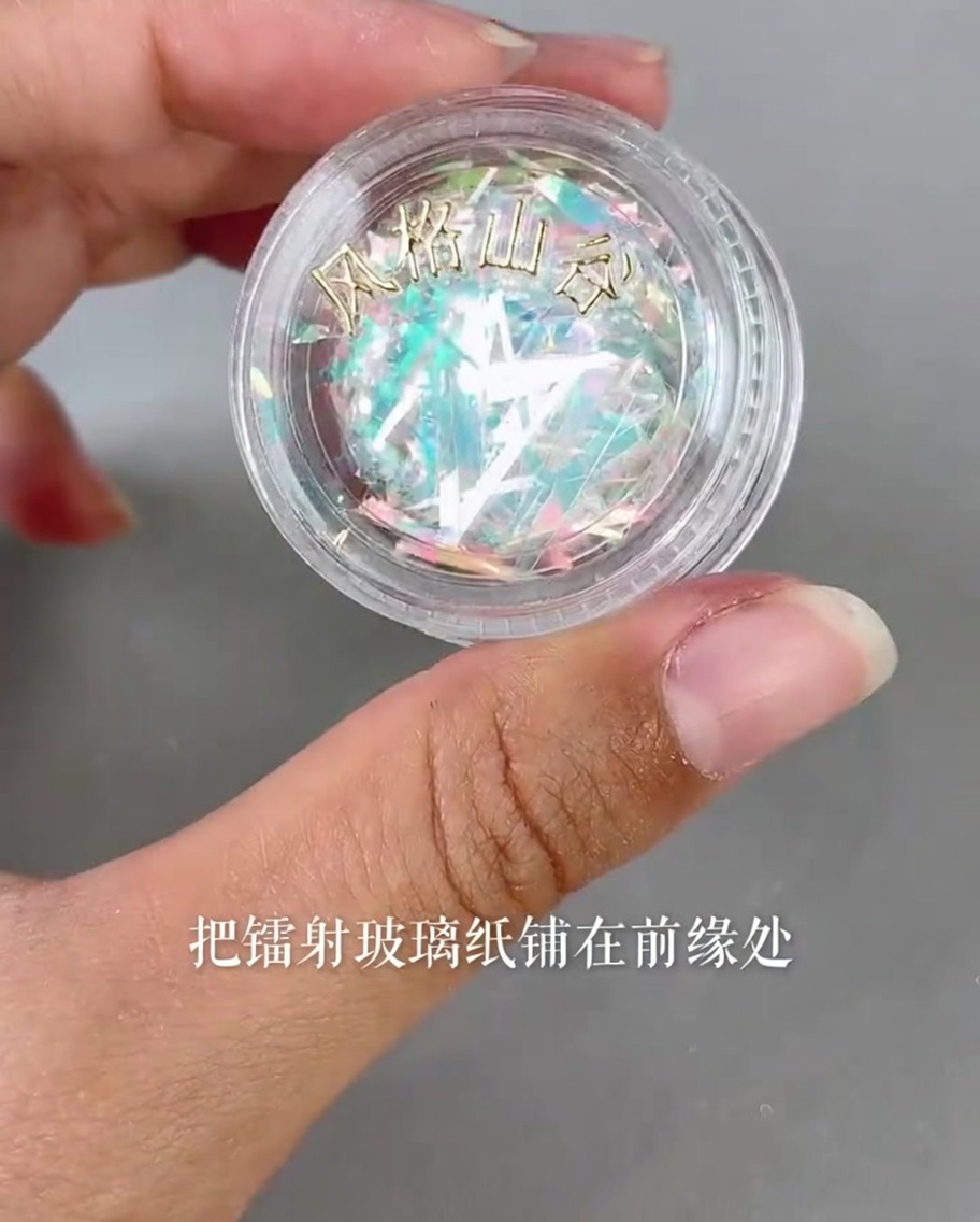 Pequeños trozos de papel de cristal láser iridiscente colocándose en el borde de un tip usando una herramienta de precisión.