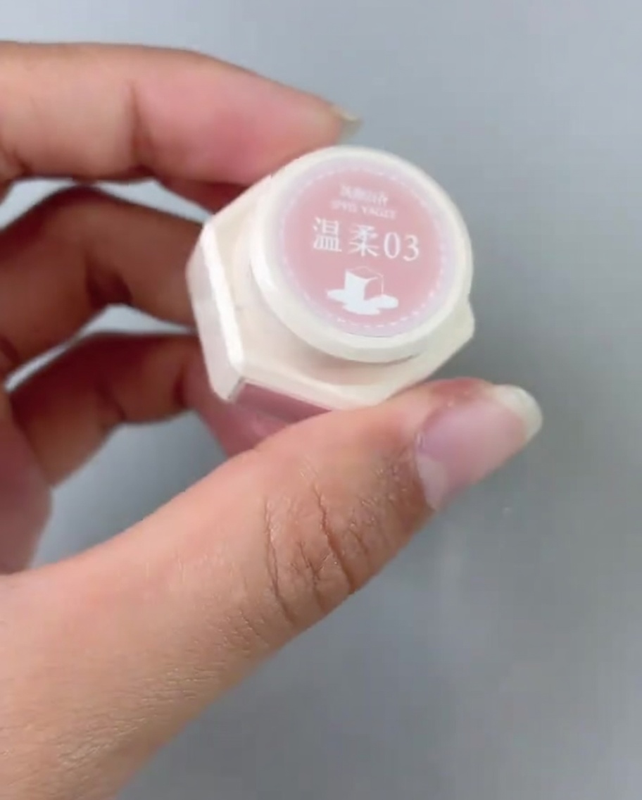 Un pincel aplicando una capa de esmalte en gel rosa en la zona de la base de un tip.