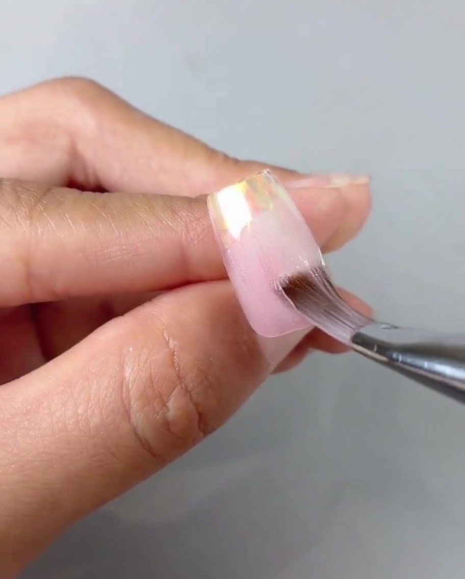 Primer plano de un pincel suavizando y difuminando el gel rosa translúcido en un tip.
