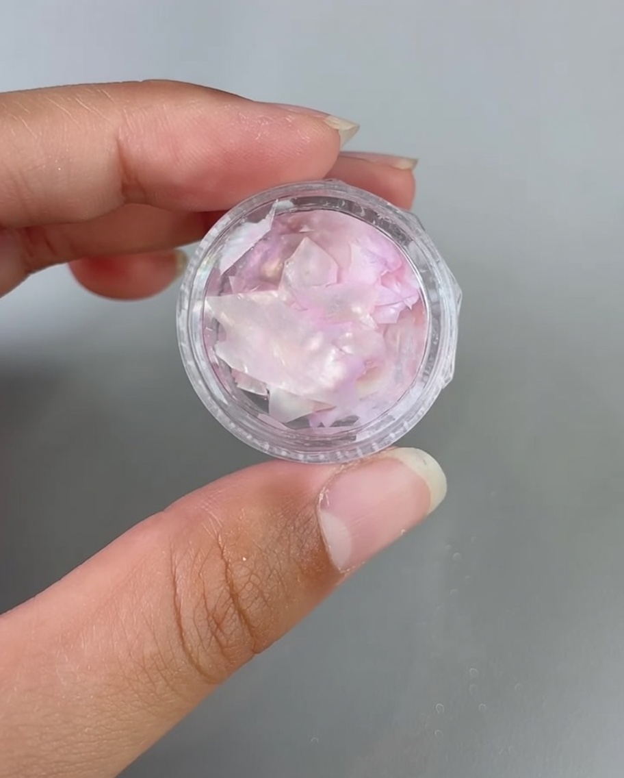 Unas pinzas colocando fragmentos de nácar iridiscente sobre una uña cubierta con gel.