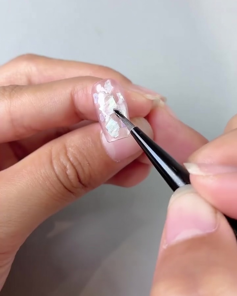 Un pincel difuminando gel blanco lechoso en las esquinas de una uña rosa con efecto ojo de gato.