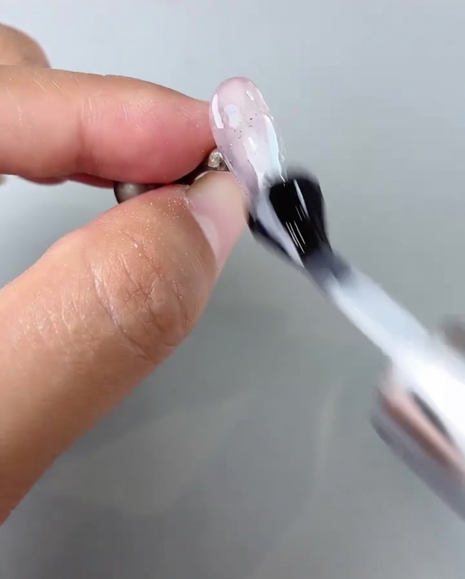 Un pincel aplicando una capa de brillo final sobre el diseño de uñas terminado.