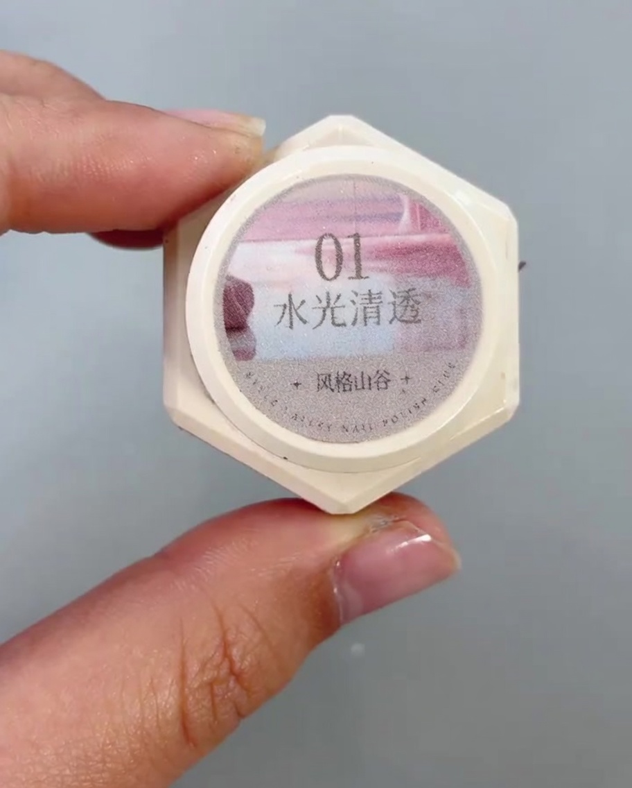 Un pincel de uñas aplicando un gel ojo de gato transparente y brillante en la mitad inferior de una uña.