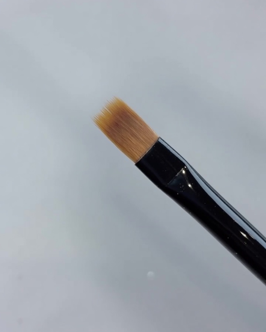 Un primer plano de un pincel de barrido extendiendo el esmalte de gel hacia adelante para difuminar y crear un degradado.