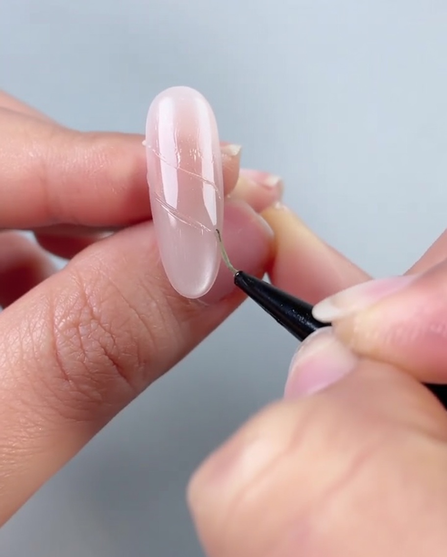 Una uña mostrando una línea de pequeñas perlas blancas y diamantes transparentes siendo colocados sobre líneas de pegamento adhesivo.