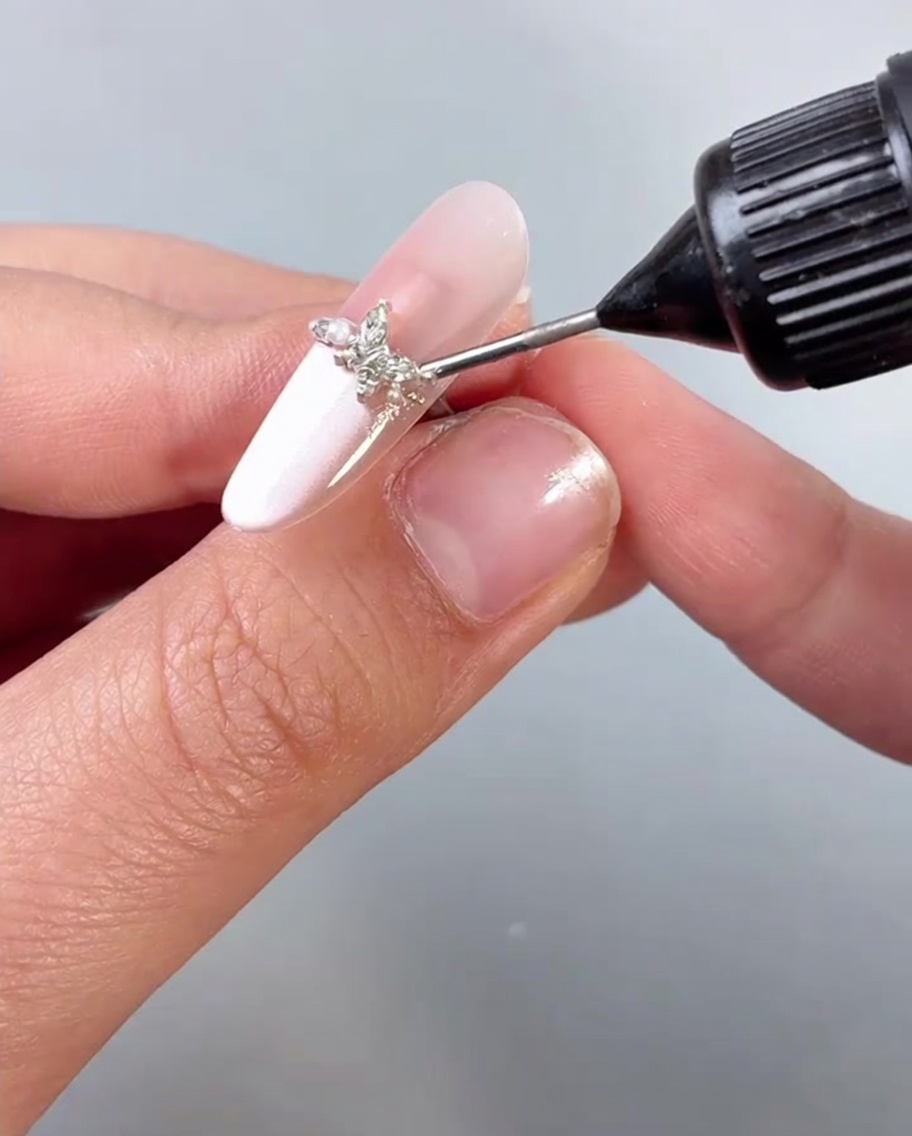 Aplicando un top coat o sellador transparente sobre una uña adornada con un encanto de mariposa.