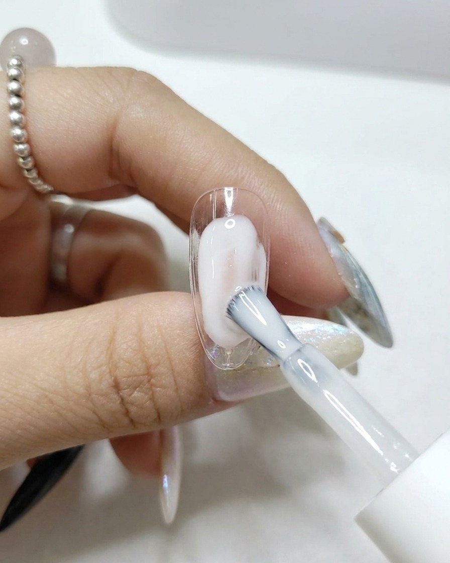 Un pincel aplicando un top coat transparente y brillante sobre una uña postiza.