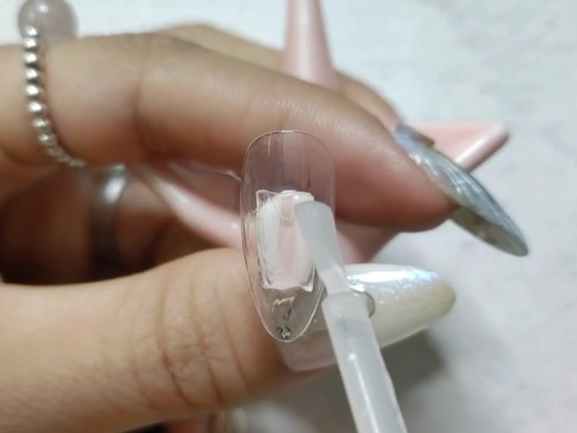 Una uña postiza colocada dentro de una lámpara UV/LED pequeña para el curado.