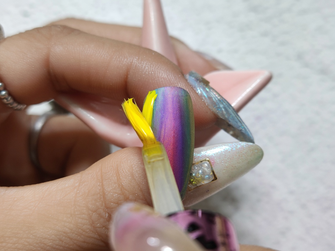 Un pincel aplicando un top coat transparente y brillante sobre un diseño de uñas con degradado de acuarela terminado.