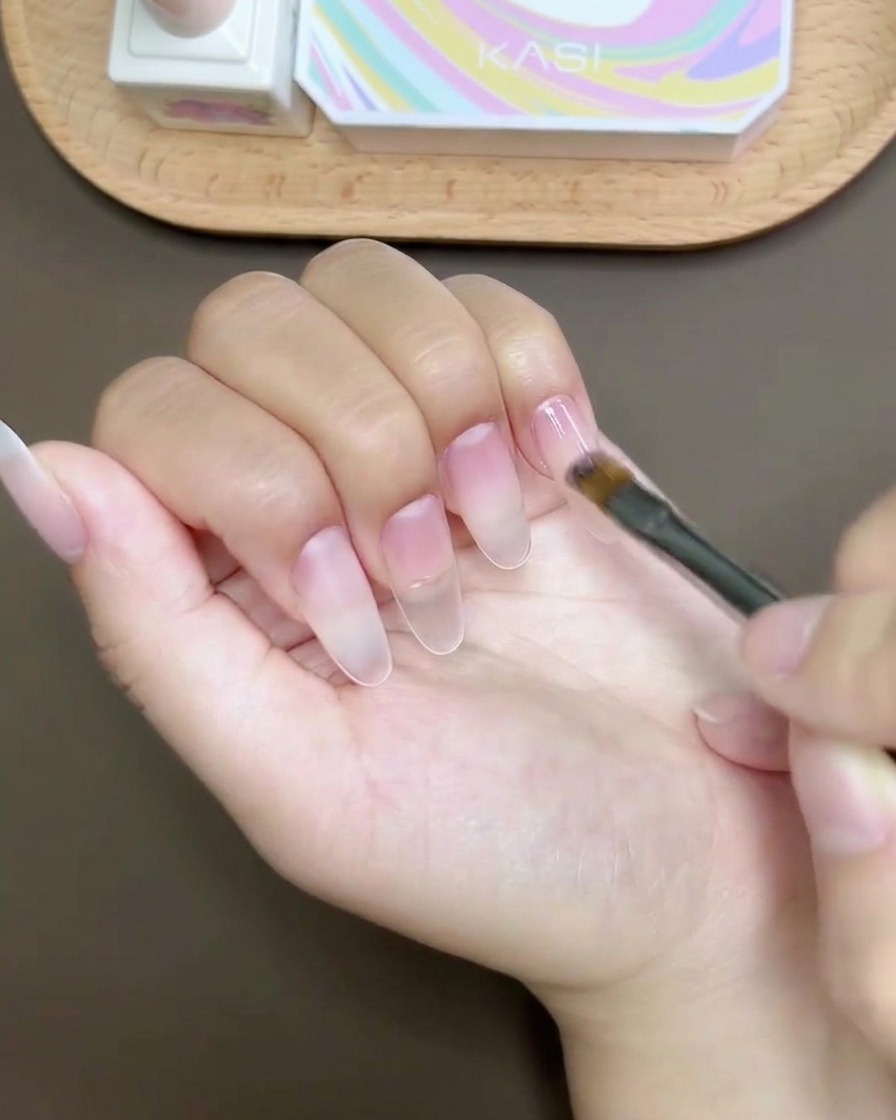 Un pincel de gel aplicando un top coat brillante y suave sobre un diseño de uñas terminado.