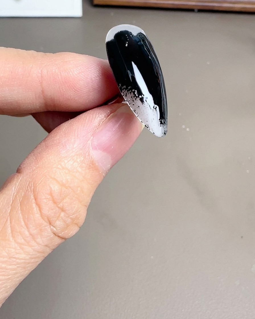 Primer plano de un pincel aplicando esmalte de gel negro brillante sobre un tip de uña stiletto transparente.