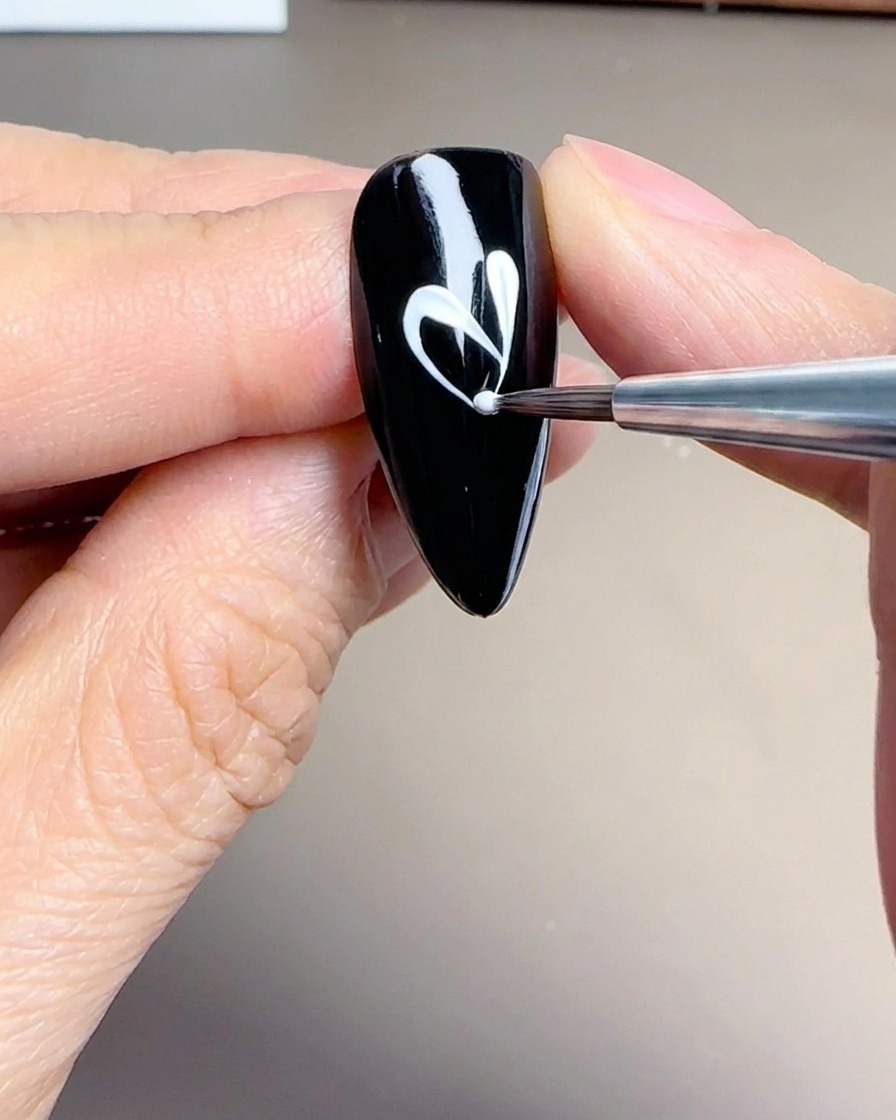 Primer plano de un pincel liner creando pétalos blancos delicados y alargados sobre una base negra.