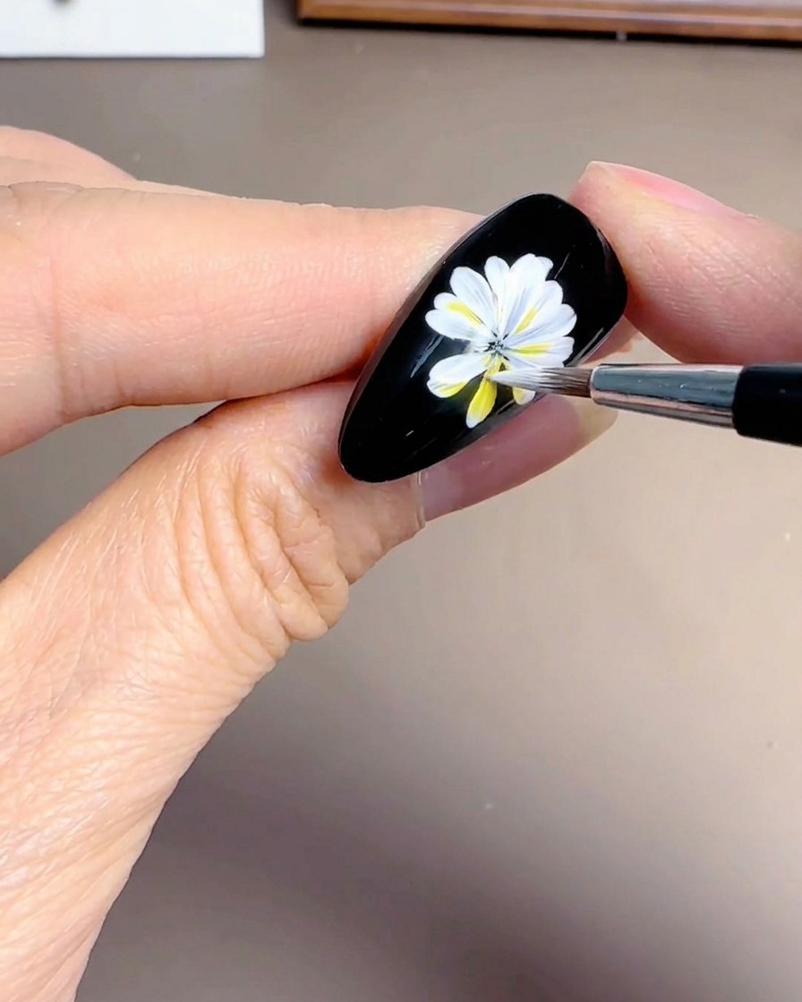 Primer plano de una mano añadiendo pétalos blancos superpuestos a un diseño de margarita sobre base negra.