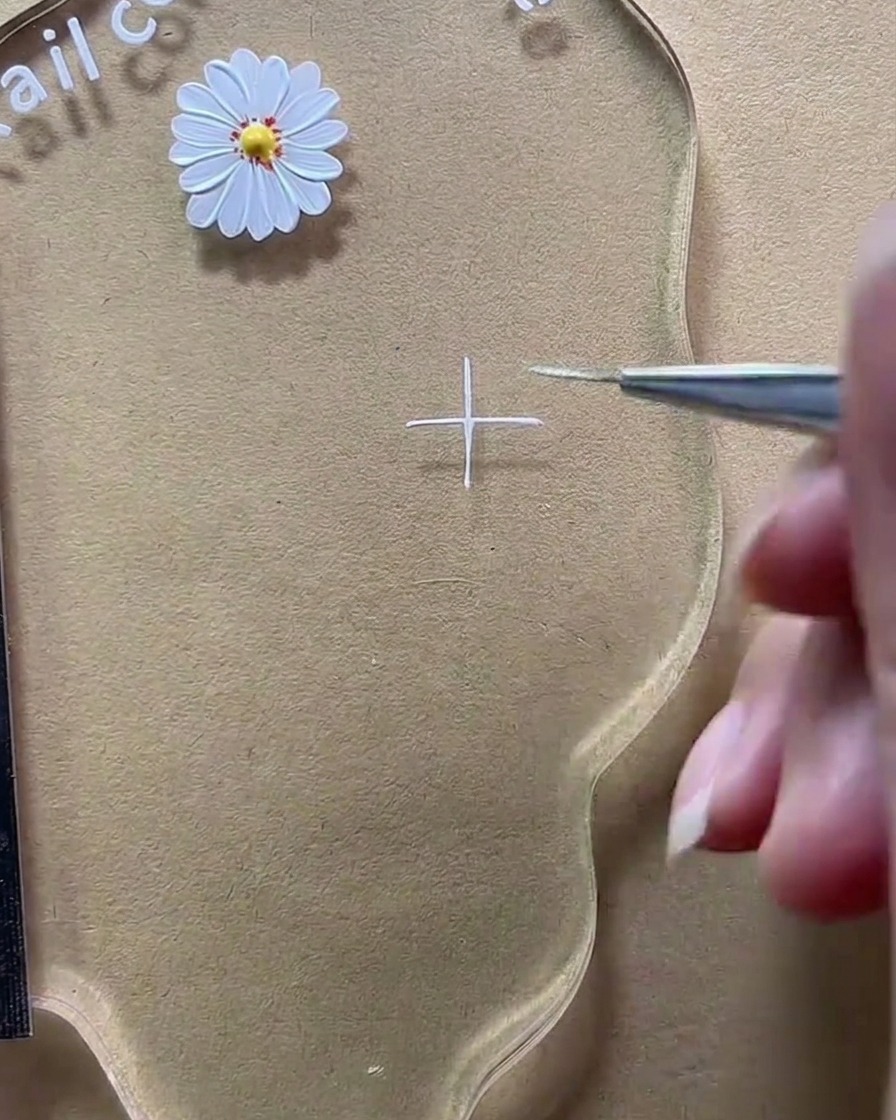 Primer plano de un pincel completando un signo más blanco en la paleta transparente.