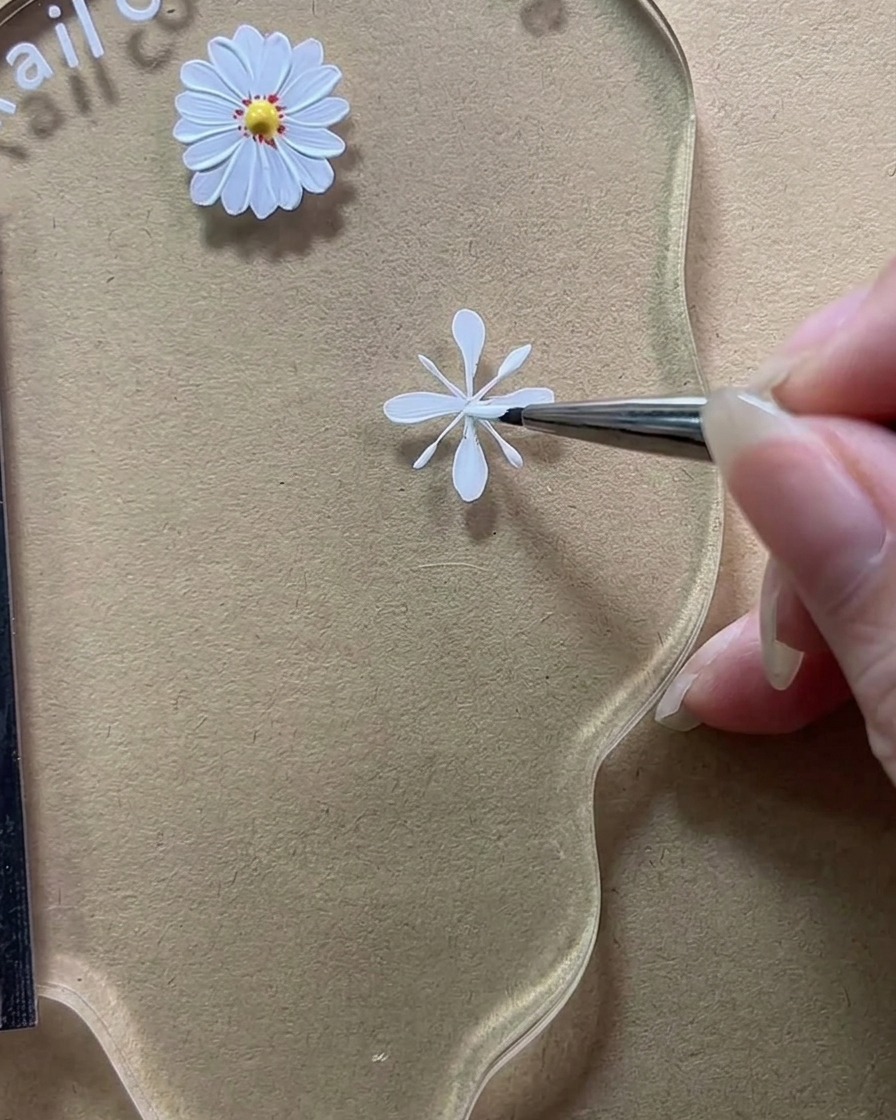 Primer plano de un pincel rellenando las líneas guía verticales para crear pétalos blancos opacos y completos.