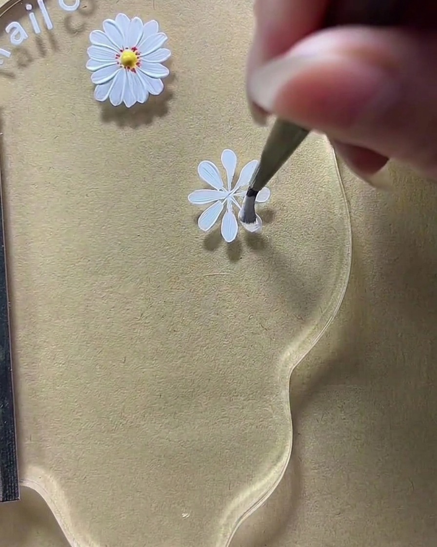 Primer plano de una paleta de nail art donde un pincel está ensanchando las formas de pétalos blancos en un diseño de margarita.
