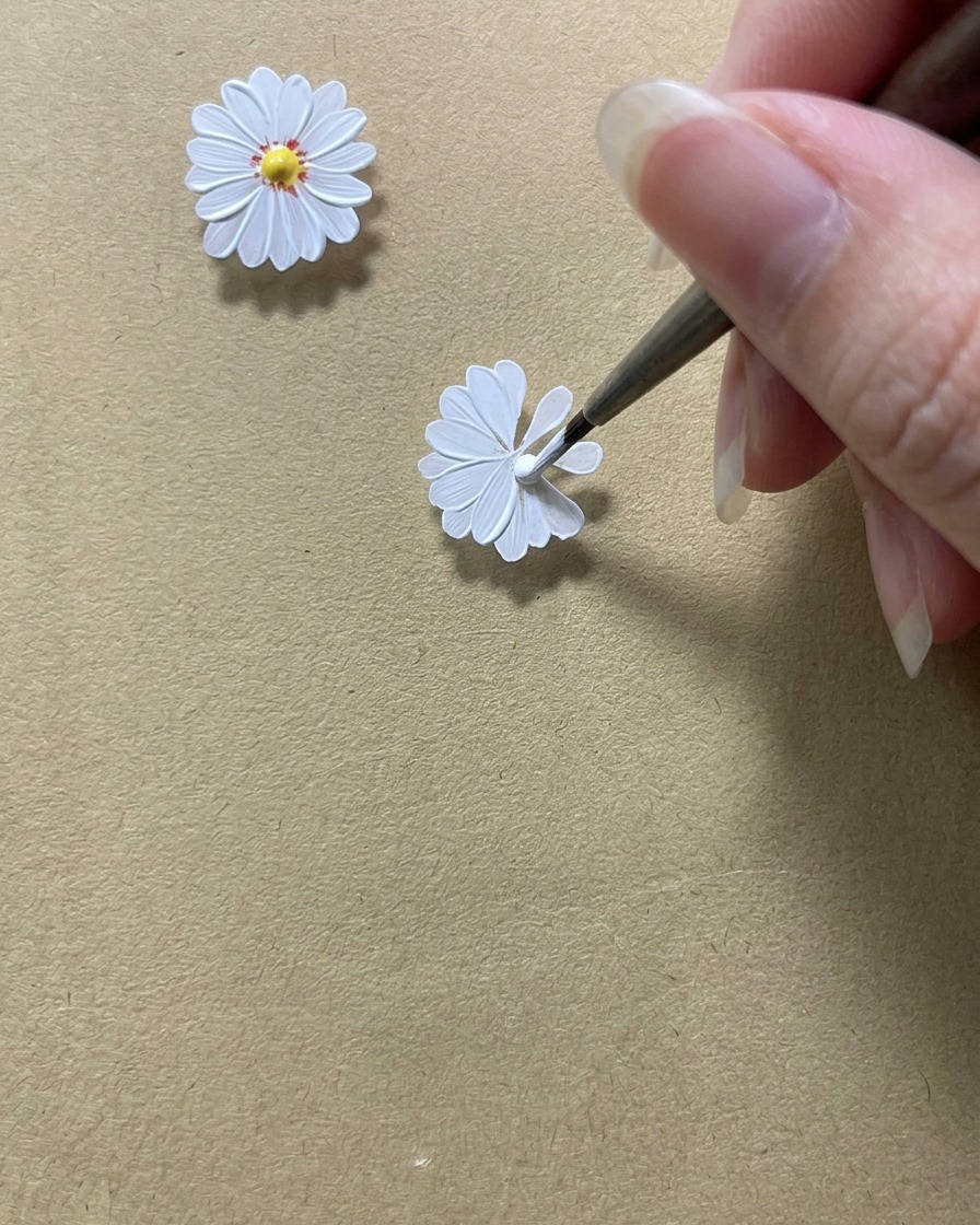 Un pincel de detalle perfeccionando los bordes internos de los pétalos de la margarita blanca para crear un espacio circular en el medio.