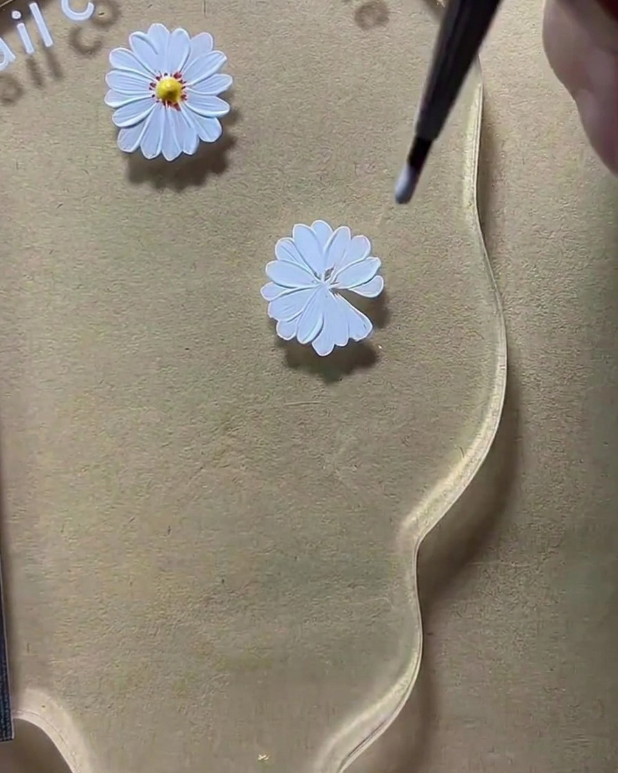 Una herramienta de punteado colocando un punto central amarillo sobre un diseño de pétalo de margarita blanca.
