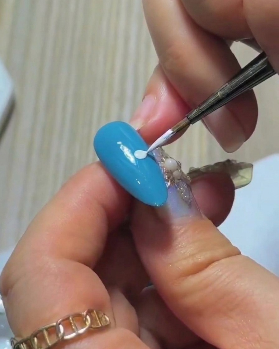 Primer plano de la punta de un pincel liner sumergiéndose en una pequeña cantidad de esmalte de gel blanco en una paleta.