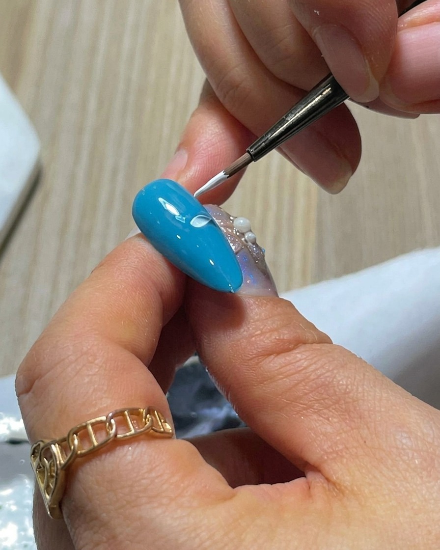 Primer plano de una uña azul con dos pétalos de gel blanco pintados uno al lado del otro usando la técnica de presionar y levantar.
