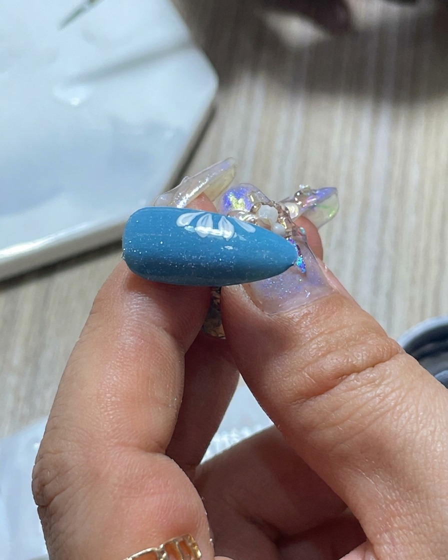 Primer plano de un pincel de arte de uñas siendo limpiado en una paleta para controlar la cantidad de esmalte de gel blanco.