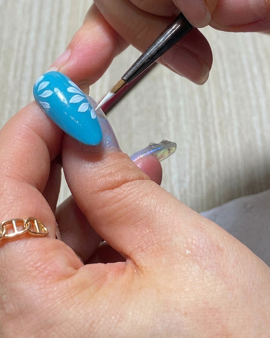 La punta de un pincel liner aplicando un pétalo blanco audaz y opaco para la segunda capa de un diseño de margarita.