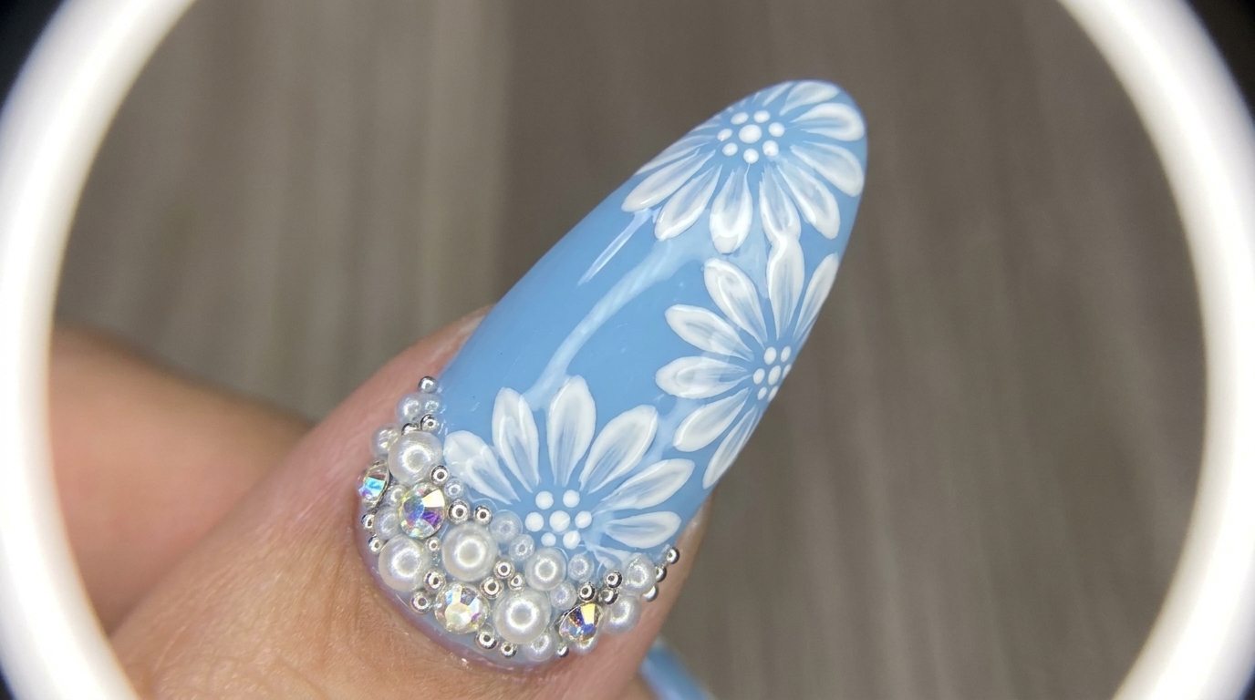 Arte de uñas floral con margaritas blancas de doble capa pintadas a mano sobre una base azul claro brillante, decoradas con cristales y perlas.
