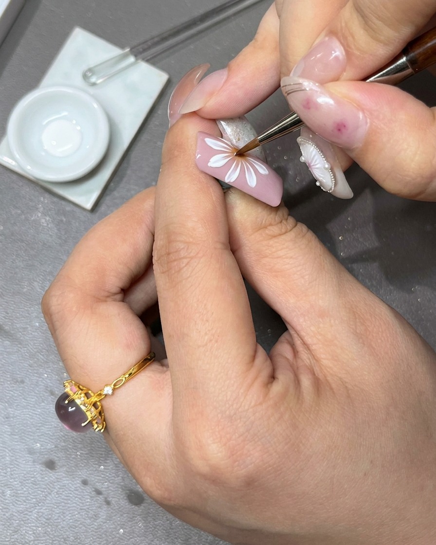 Un pincel aplicando una segunda capa de pétalos de gel blanco sobre la capa inicial de la flor para añadir profundidad.