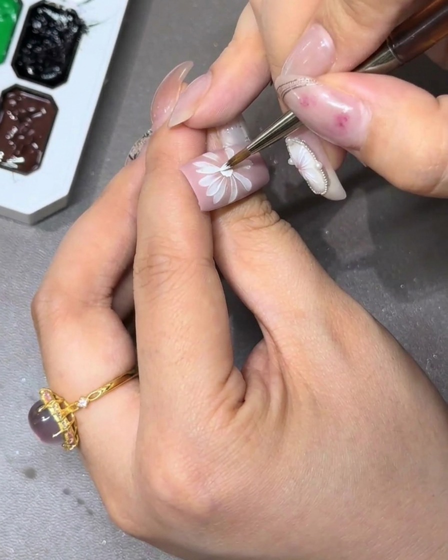 Primer plano de una uña siendo decorada con un diseño de flor blanca de varias capas completo.