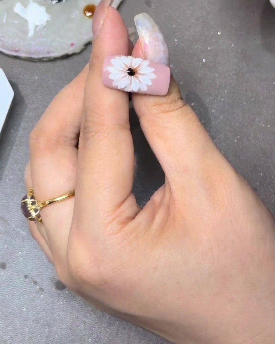 Un pincel delineador creando detalles finos de estambres amarillos que irradian desde el centro de la flor.