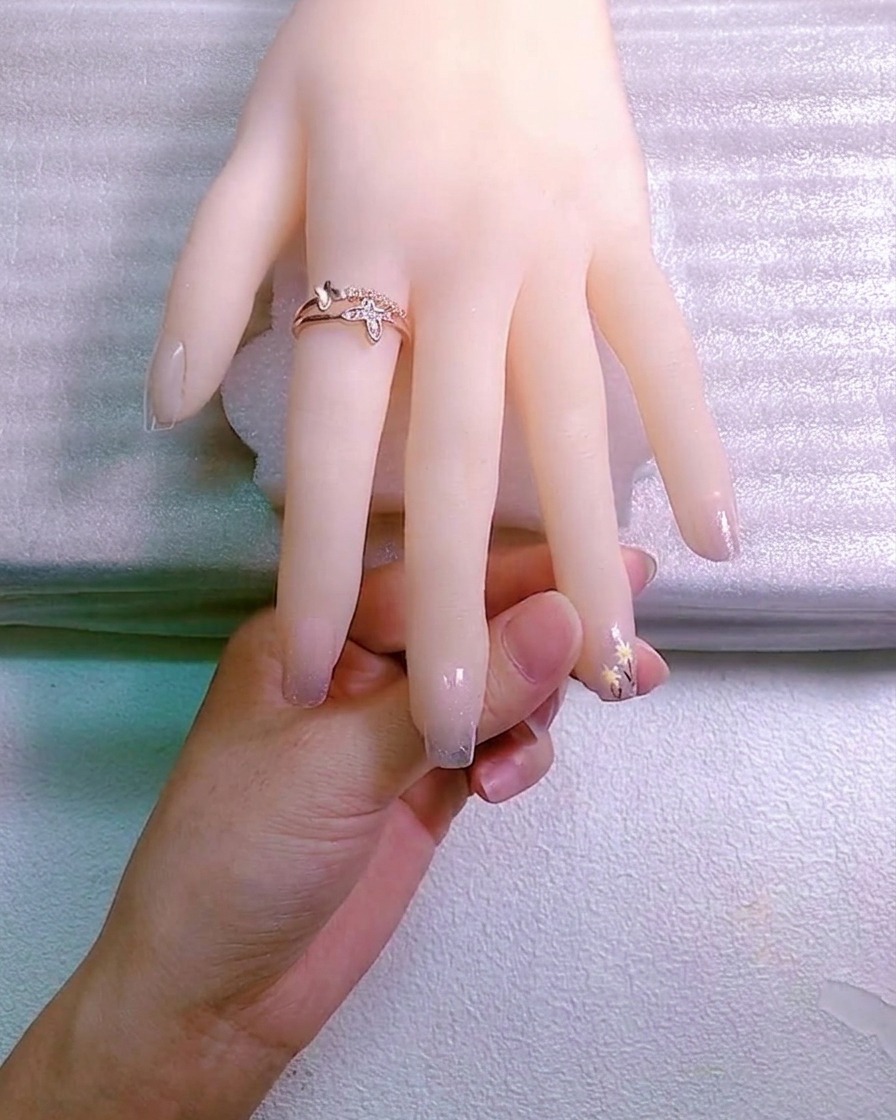 Un artista de uñas usando una herramienta para colocar un pequeño adorno de cristal en una gota de gel adhesivo sobre una uña.