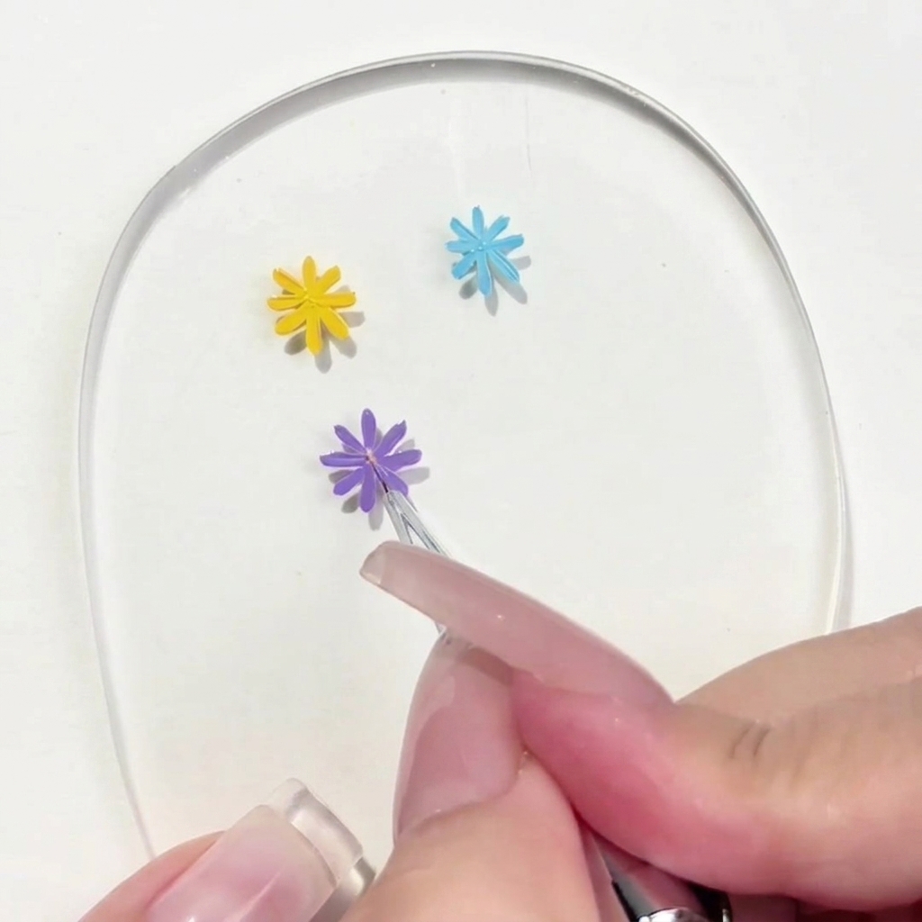 Un primer plano de un pincel de detalle colocando un pequeño punto amarillo en el centro de una margarita morada pintada a mano.