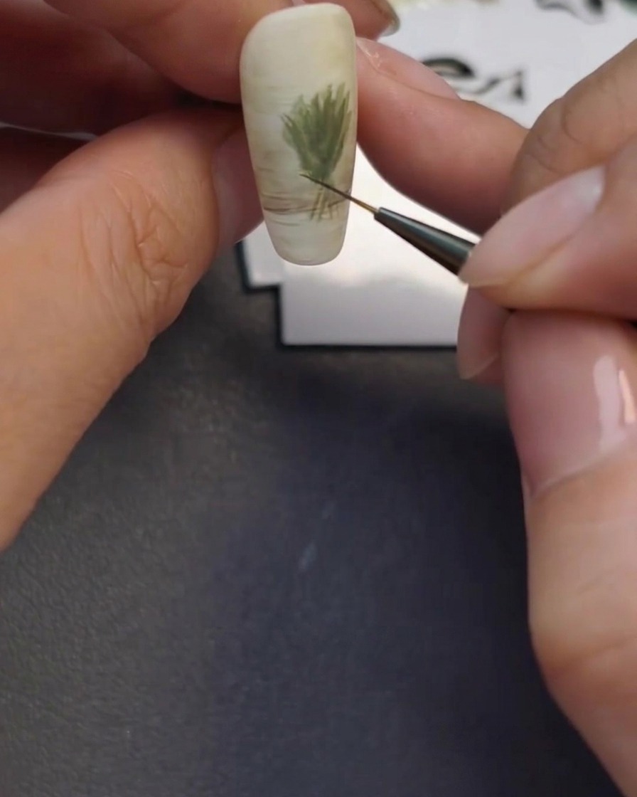 Un pincel fino creando el contorno sutil de un jarrón de cristal en la base del diseño.