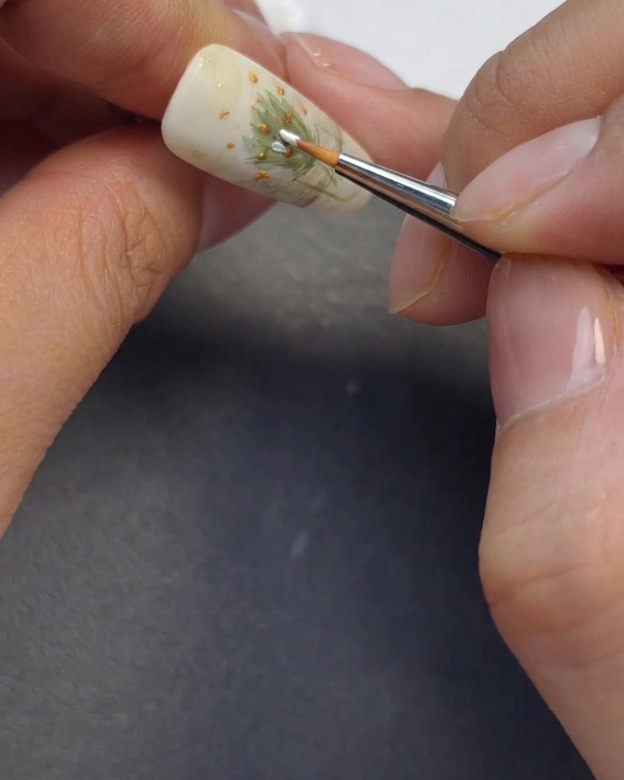 Un pincel fino pintando pétalos de margarita blancos alrededor de los centros.