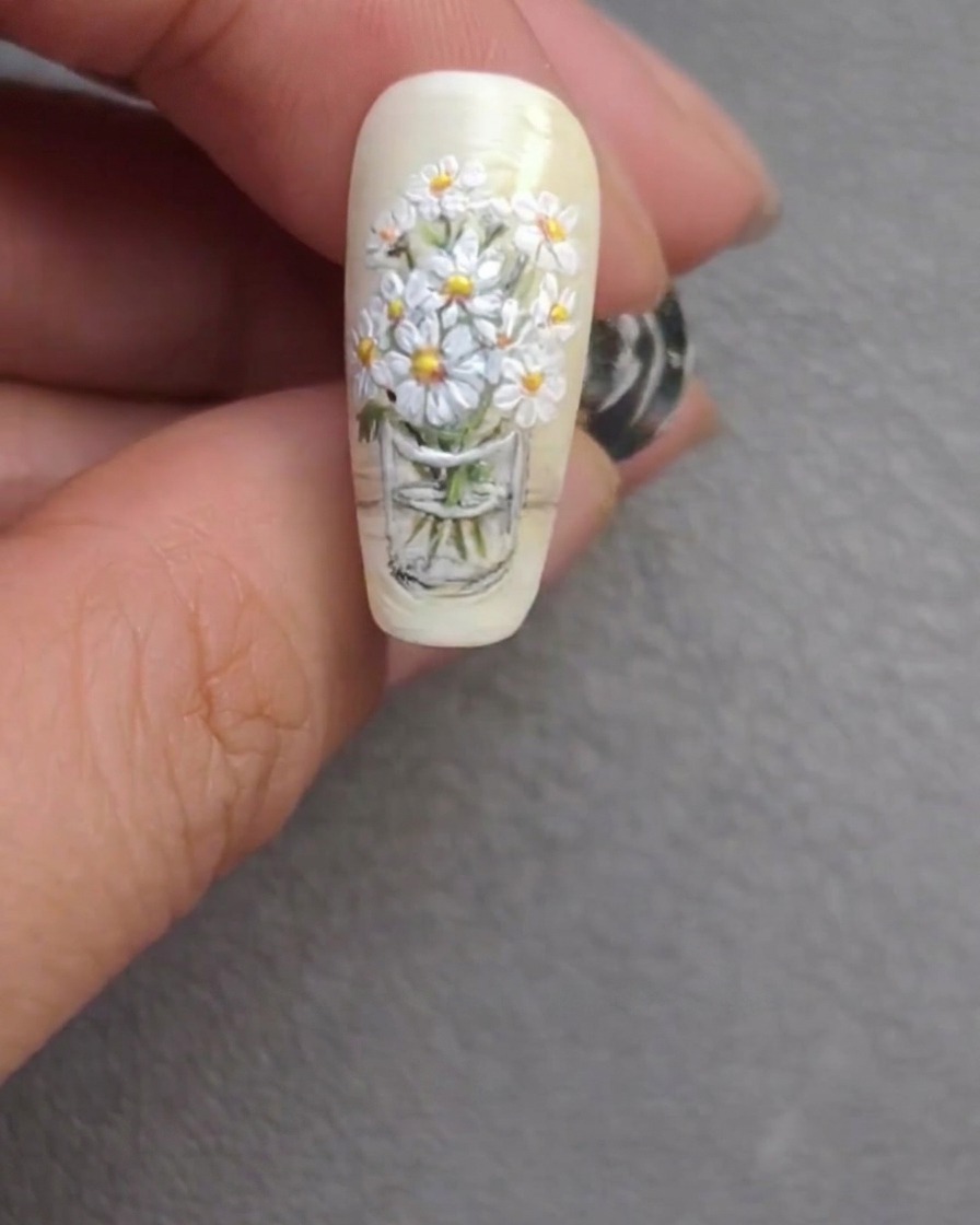 El diseño de uñas terminado con ramo de margaritas, mostrando tallos refinados y reflejos brillantes.