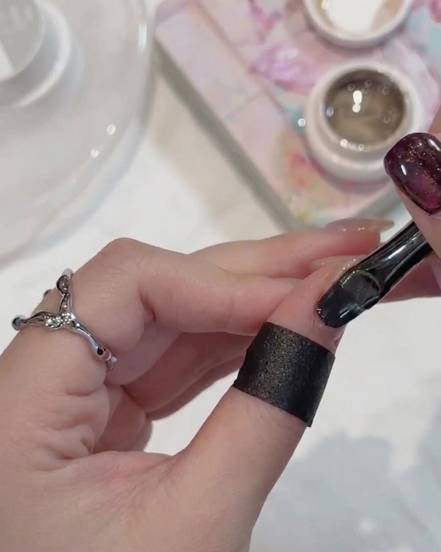Un pincel de uñas aplicando gel cat-eye brillante oscuro sobre una uña.