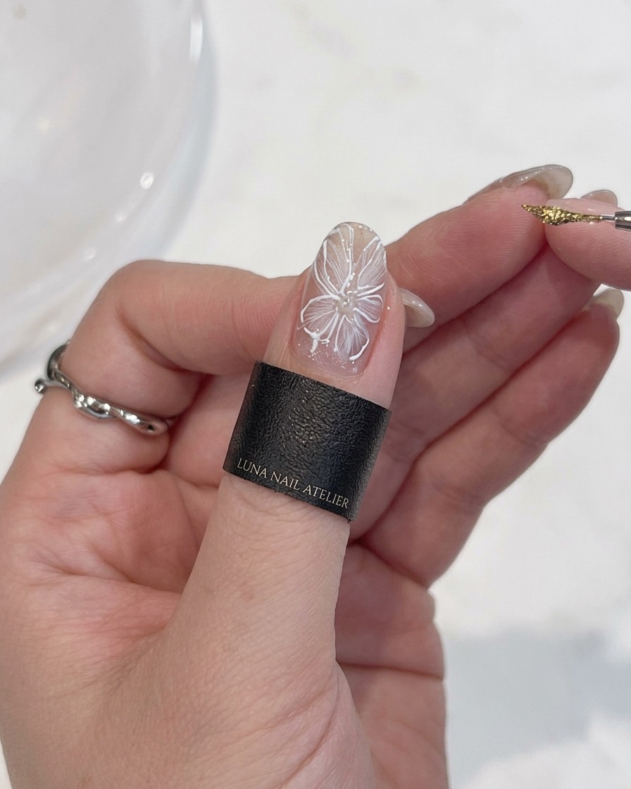 Primer plano de una mano con un pincel de detalle, aplicando un punto preciso de gel metálico dorado en el centro de una flor blanca.