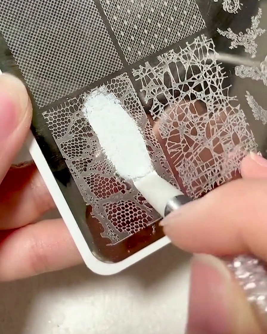 Un raspador de plástico siendo utilizado para limpiar el exceso de gel de una placa de estampado de encaje.