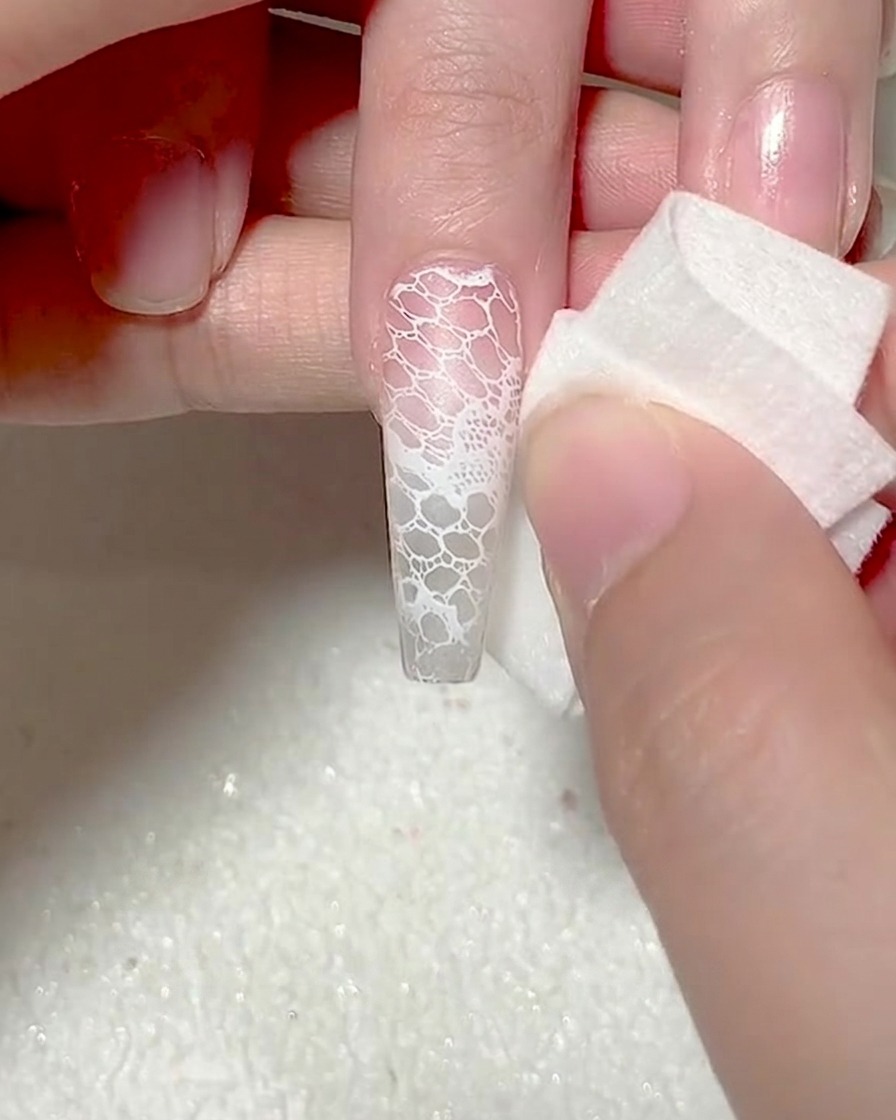 Primer plano de una esponja de maquillaje blanca aplicando gel blanco en la punta de una uña para crear un efecto ombré.